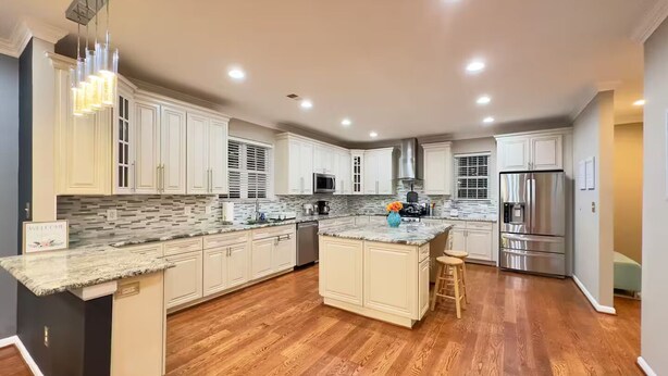 Una cocina amplia con gabinetes blancos, encimera de granito y refrigerador de acero inoxidable.