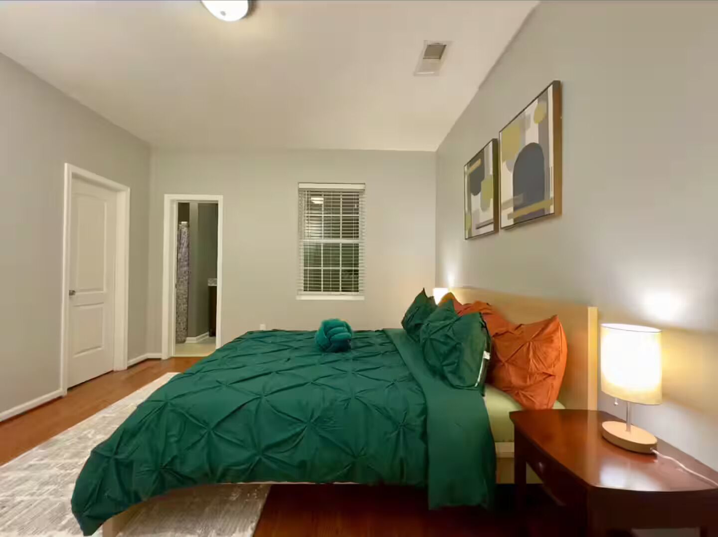 Een slaapkamer met een bed, nachtkastje met lamp, raam met zonwering en een deur.