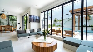 Una sala de estar moderna con un sofá modular, una mesa de centro redonda de madera y ventanas amplias que dan a un paisaje exterior.
