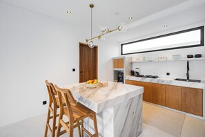Een moderne keuken met een marmeren eiland, houten stoelen, een fruitschaal en een hanglamp.