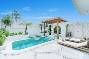 Un espace piscine comprenant des chaises longues, un jacuzzi et une pergola.