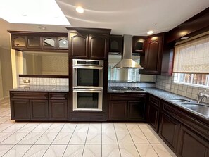 A kitchen with dark wood cabinets, a double oven, a stainless steel range, and a window with blinds. - Spacious Beauty in West San Jose — Family-Friendly Comfort with Late Checkout (San Jose)
