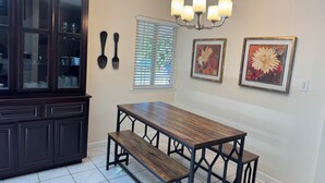 Un coin repas avec une table et des bancs en bois foncé, une vitrine, un lustre et deux tableaux floraux encadrés accrochés au mur.