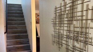 Un couloir avec un escalier en bois et une œuvre d’art en métal fixée au mur.