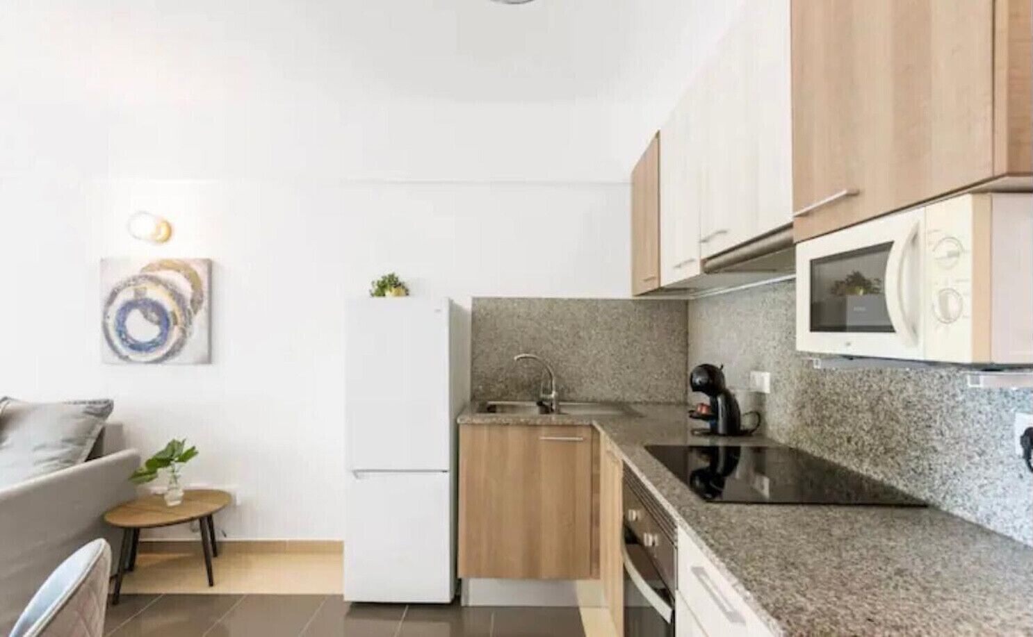 Een moderne keuken met granieten aanrechtbladen, houten kasten, een ingebouwde magnetron en een kleine eethoek met een tafel en stoelen.