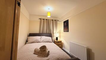 A bedroom with a bed, a nightstand, a lamp, a radiator, and a painting on the wall.