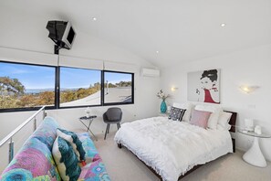 A modern bedroom with a large bed, a desk, and a chair. There are three windows providing a view of the outdoors. - Blue Datcha (Aireys Inlet)