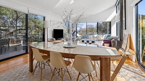 Een moderne woonkamer met een glazen eettafel, comfortabele zitplaatsen en een groot raam met uitzicht op de omgeving.