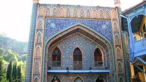 Un bâtiment dont la façade présente un motif bleu et or, avec des fenêtres en arc de cercle et un balcon doté d’une balustrade en métal.
