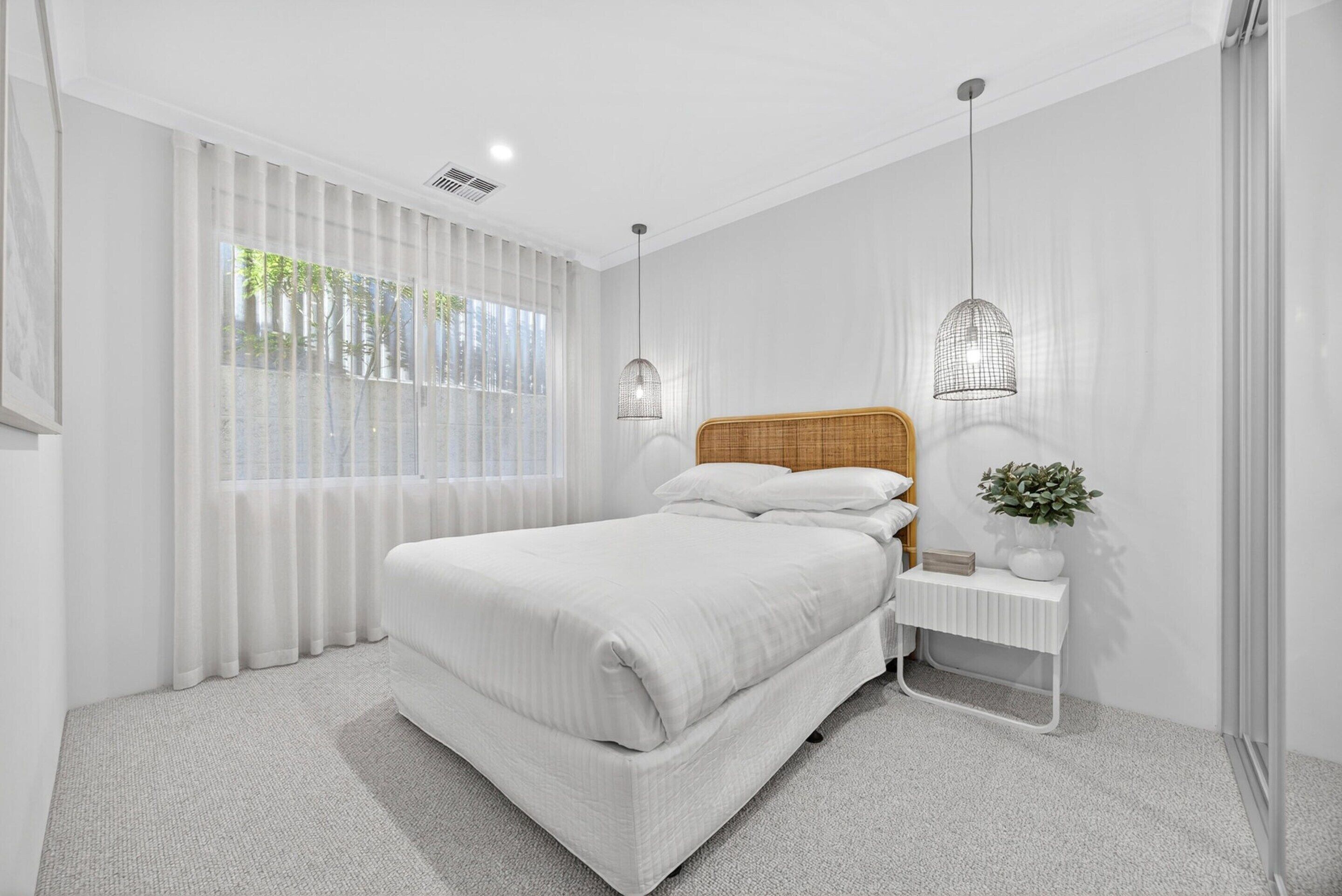 Ein modernes Schlafzimmer mit einem großen Bett, weißen Vorhängen und zwei Pendelleuchten.