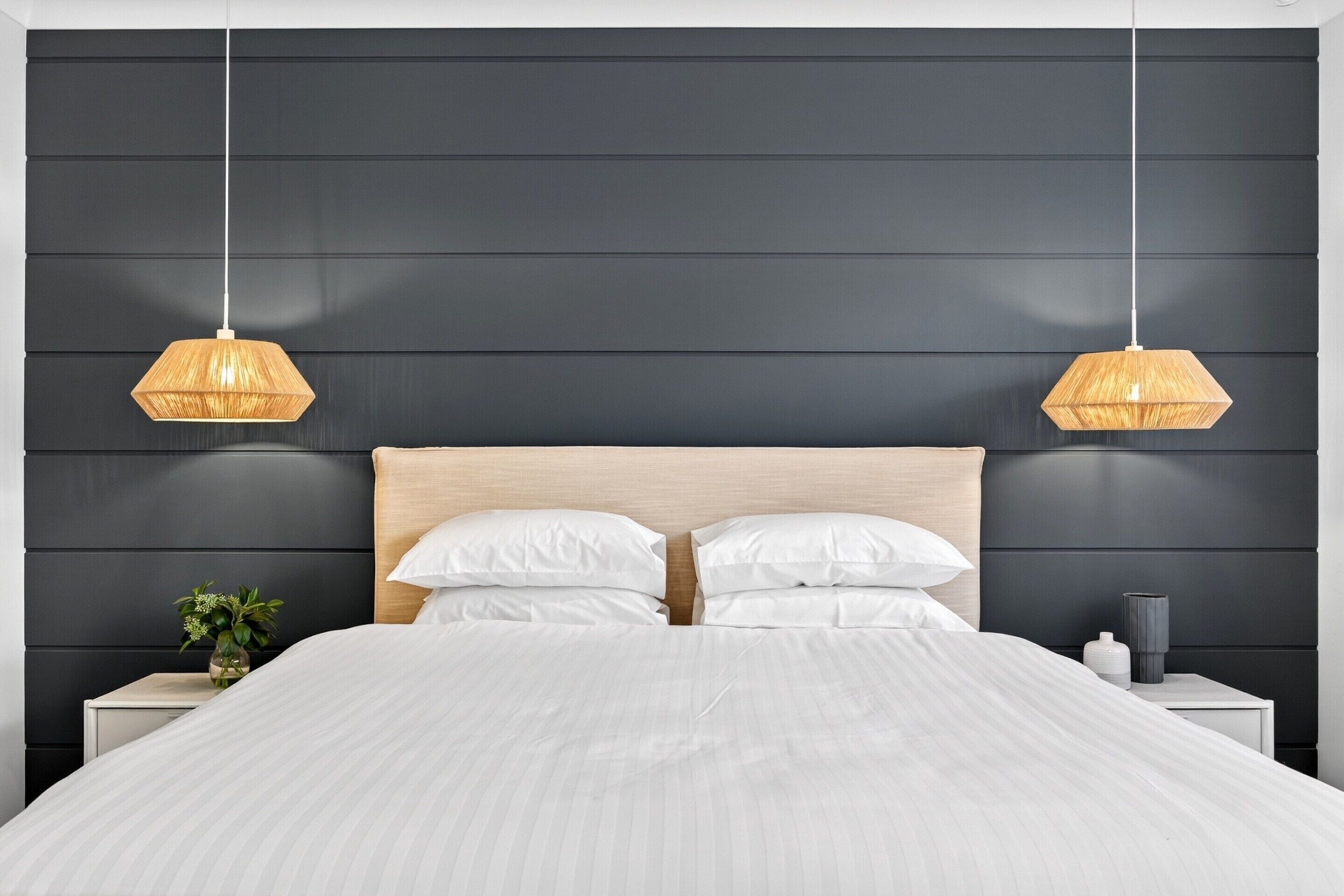 A modern bedroom with a large bed, dark wall paneling, and two hanging light fixtures.