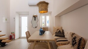 Un coin repas avec une table, des chaises et une suspension lumineuse en forme de panier. On y trouve également un extincteur et un miroir accroché au mur.