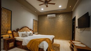 Une chambre dotée d’un grand lit, de tables de chevet en bois, d’un ventilateur de plafond, d’un climatiseur et d’un téléviseur fixé au mur.