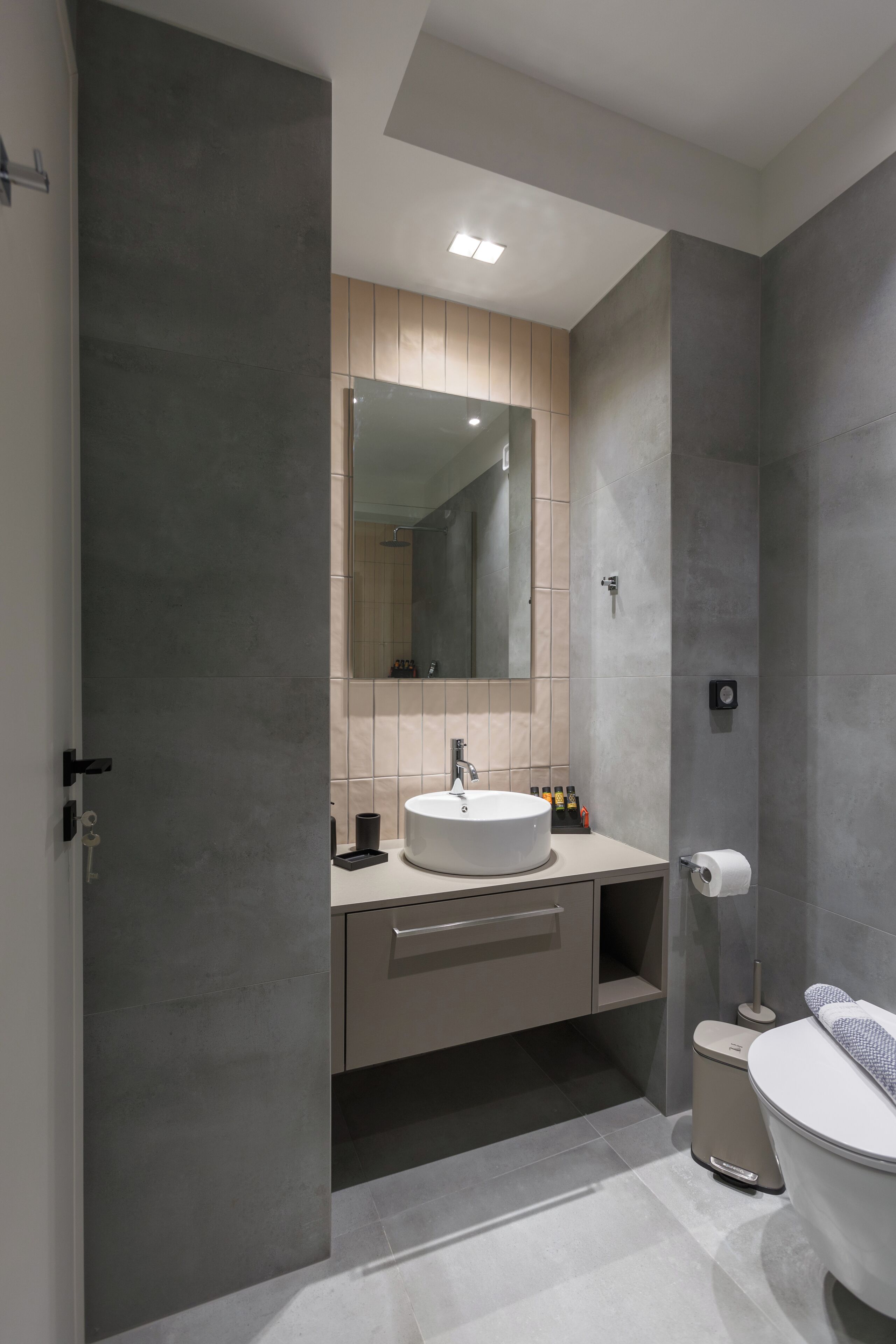 A modern bathroom with a large mirror, a round sink, a toilet, and a cabinet.