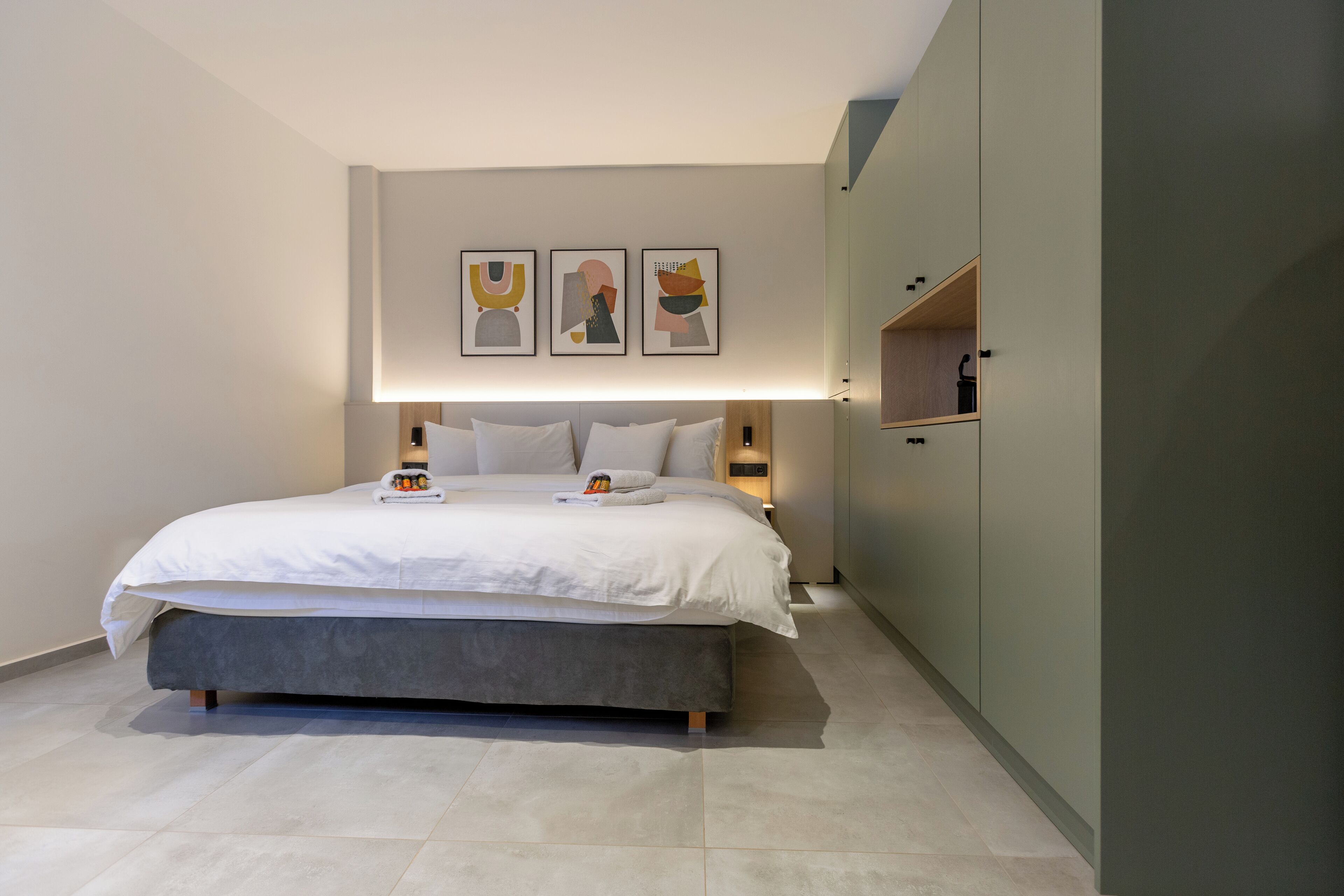A modern bedroom with a large bed, bedside tables, a wardrobe, and abstract wall art.