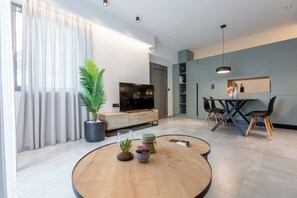 Una sala de estar moderna con televisor, comedor y un amplio ventanal con cortinas.