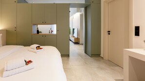 A modern hotel room with a large bed, a built-in wardrobe, a small seating area, and a bathroom with a white sink. - 2 Independent Apts with Yard near the City's Heart (Kalamata)