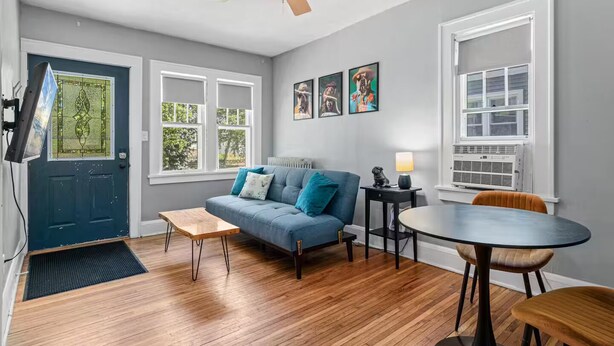 Een woonkamer met een blauwe bank, een houten salontafel, een ronde tafel en een plafondventilator.