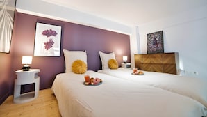 Ett hotellrum med två sängar, ett trägolv, en accentvägg i lila färg och konstverk på väggarna.