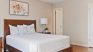 Une chambre avec un lit en bois, un ventilateur de plafond, une table de chevet avec une lampe et un tableau encadré au mur.