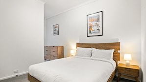 A neatly made bed with white linens, a wooden headboard, and two bedside lamps. - Peaceful 2-bed Apartment With Gym & Pool (Melbourne)