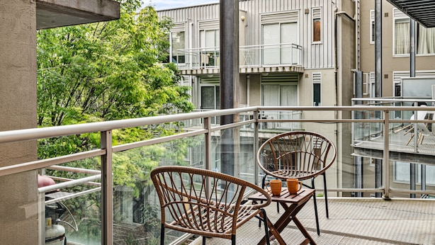 A balcony with wicker chairs and a table, overlooking a building with multiple windows and balconies. - Peaceful 2-bed Apartment With Gym & Pool (Melbourne)
