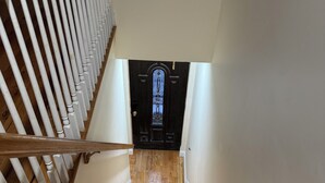 A wooden staircase with a white railing leading to a dark door with a decorative glass panel.