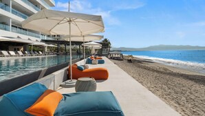 Un hotel frente a la playa con piscina, sillas de descanso y sombrillas.