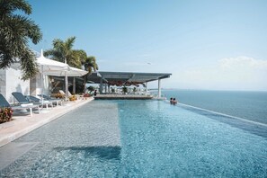 Uma piscina infinita com água cristalina, espreguiçadeiras e guarda-sóis, com vista para o mar.