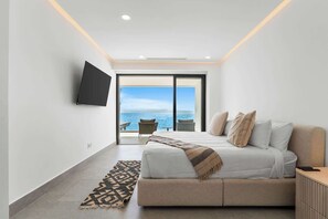 Quarto moderno com uma cama grande, televisão de tela plana e vista para o mar através de uma porta deslizante.