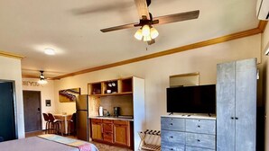 Une chambre d’hôtel comprenant un lit, un bureau avec une chaise, une kitchenette, une télévision et une armoire.