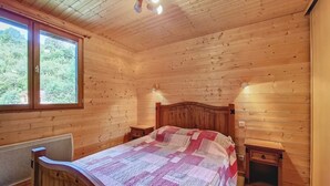 Un dormitorio de cabaña de madera con una cama, dos lámparas de noche, una ventana y un radiador.