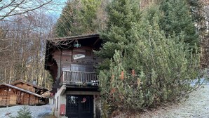 Un edificio de madera rústico con un balcón, rodeado de árboles frondosos y un camino de grava.
