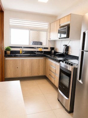 Eine moderne Küche mit Holzausbau, einem Edelstahlkühlschrank, einem eingebauten Ofen und einer Mikrowelle.