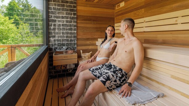A sauna room with wooden benches, a stone wall, and a window overlooking greenery. - The Lodge Transylvania (Bran)