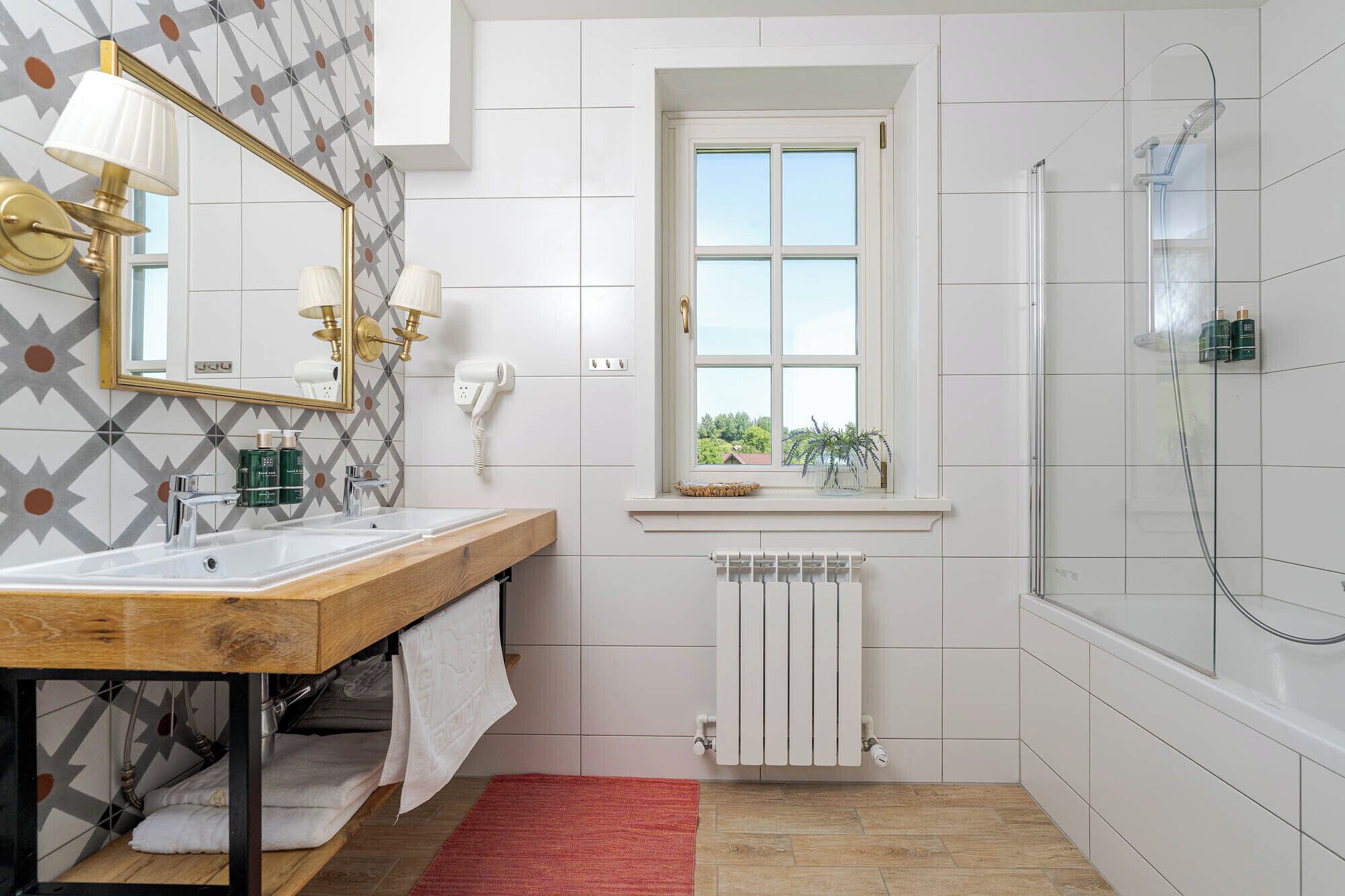 A bathroom with a wooden vanity, a large mirror, a window with a view, a shower, and a radiator.