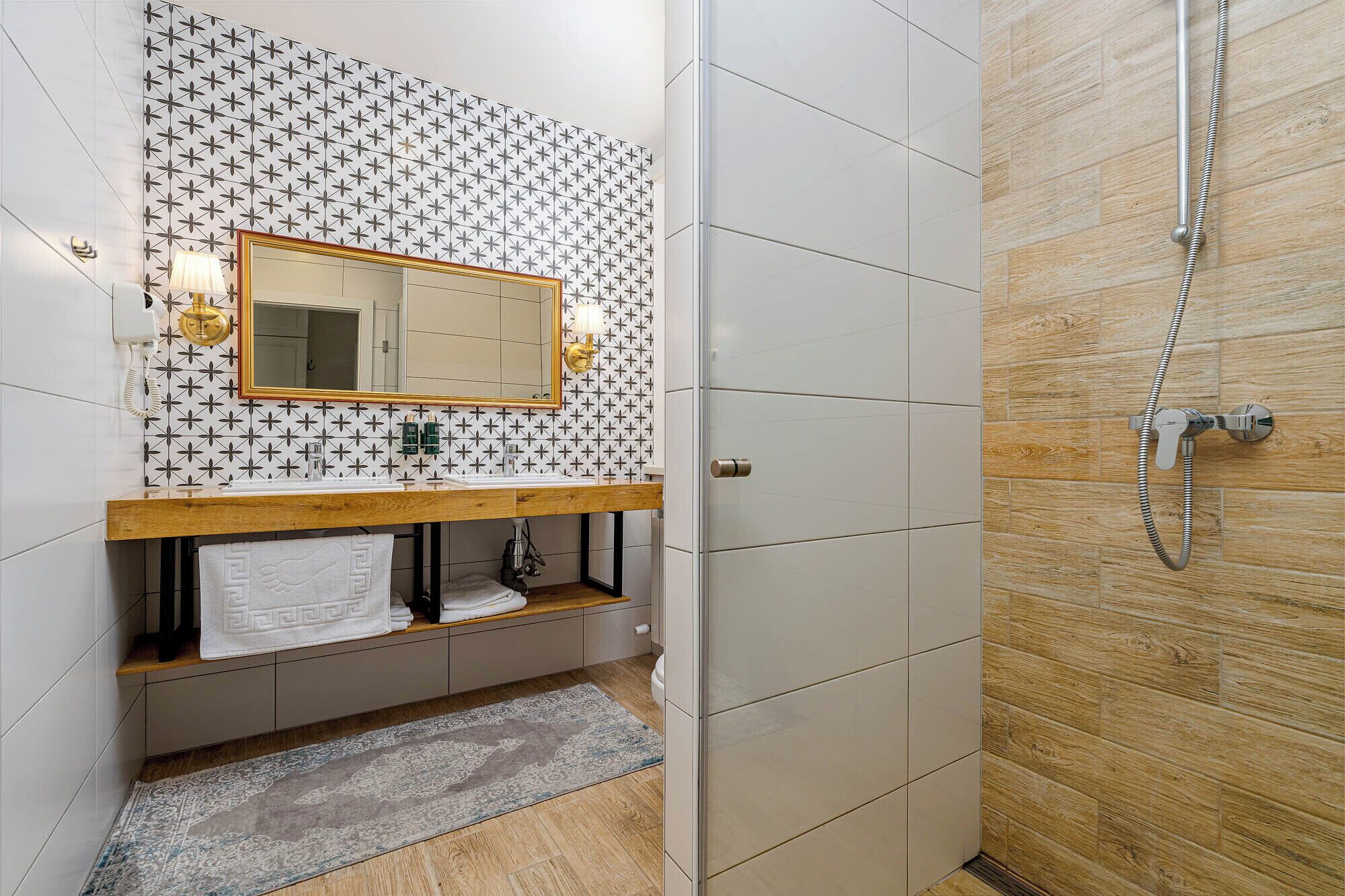 Un baño con salpicadero de azulejos, tocador de madera, espejo, perchero y zona de ducha.