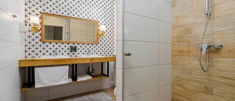 Un baño con salpicadero de azulejos, tocador de madera, espejo, perchero y zona de ducha.