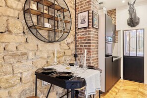 A rustic kitchen with a stone wall, a round metal shelf, and a dining table set with plates and glasses. - Charming Apartment - Paris Pere Lachaise (Paris)