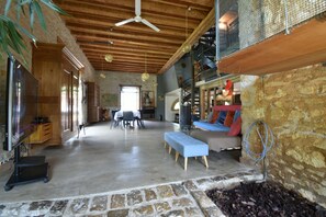 A spacious living area with a high ceiling, stone walls, and a staircase leading to an upper level. - 8-bedroom gîte, covered swimming pool and heated pool, 5000m2 green space. (Lignières)