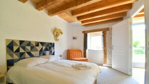 A bedroom with a large bed, a wooden ceiling, a window, and an open door leading outside. - 8-bedroom gîte, covered swimming pool and heated pool, 5000m2 green space. (Lignières)