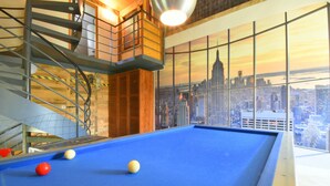 A pool table with balls, a spiral staircase, and a cityscape view through large windows. - 8-bedroom gîte, covered swimming pool and heated pool, 5000m2 green space. (Lignières)