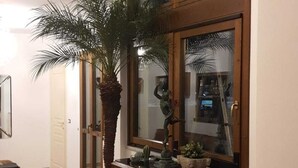 Una stanza con un'ampia finestra, un armadio in legno con decorazioni intagliate, una pianta in vaso e uno specchio appeso al muro.