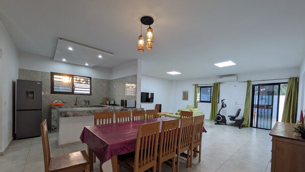 A dining area with a table and chairs, a kitchen with a refrigerator and stove, a TV, and a sliding glass door leading outside.