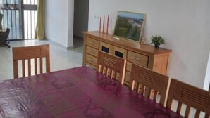 A dining area with a table covered by a purple tablecloth, wooden chairs, a wooden cabinet with a painting, and a view through a glass door.