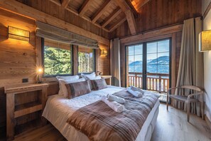 A wooden cabin bedroom with a large bed, two bedside tables, a chair, and a view of a mountainous landscape. - Chalet de l'Emey - A Lifestyle with a View of Mont Blanc (12 people) (Saint-Gervais-les-Bains)
