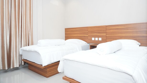 Una habitación de hotel moderna con dos camas, cabeceros de madera y un ventanal con cortinas.