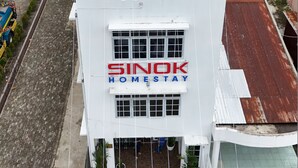 Un edificio de dos pisos con un letrero que dice "SINOK HOMESTAY".