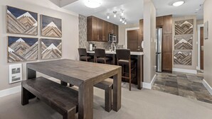 Une cuisine moderne avec des meubles de rangement en bois foncé, un îlot central doté de tabourets de bar et une table à manger avec des bancs.