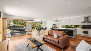 Een moderne woonkamer met open plattegrond, een eethoek, keuken en uitzicht op de omgeving.